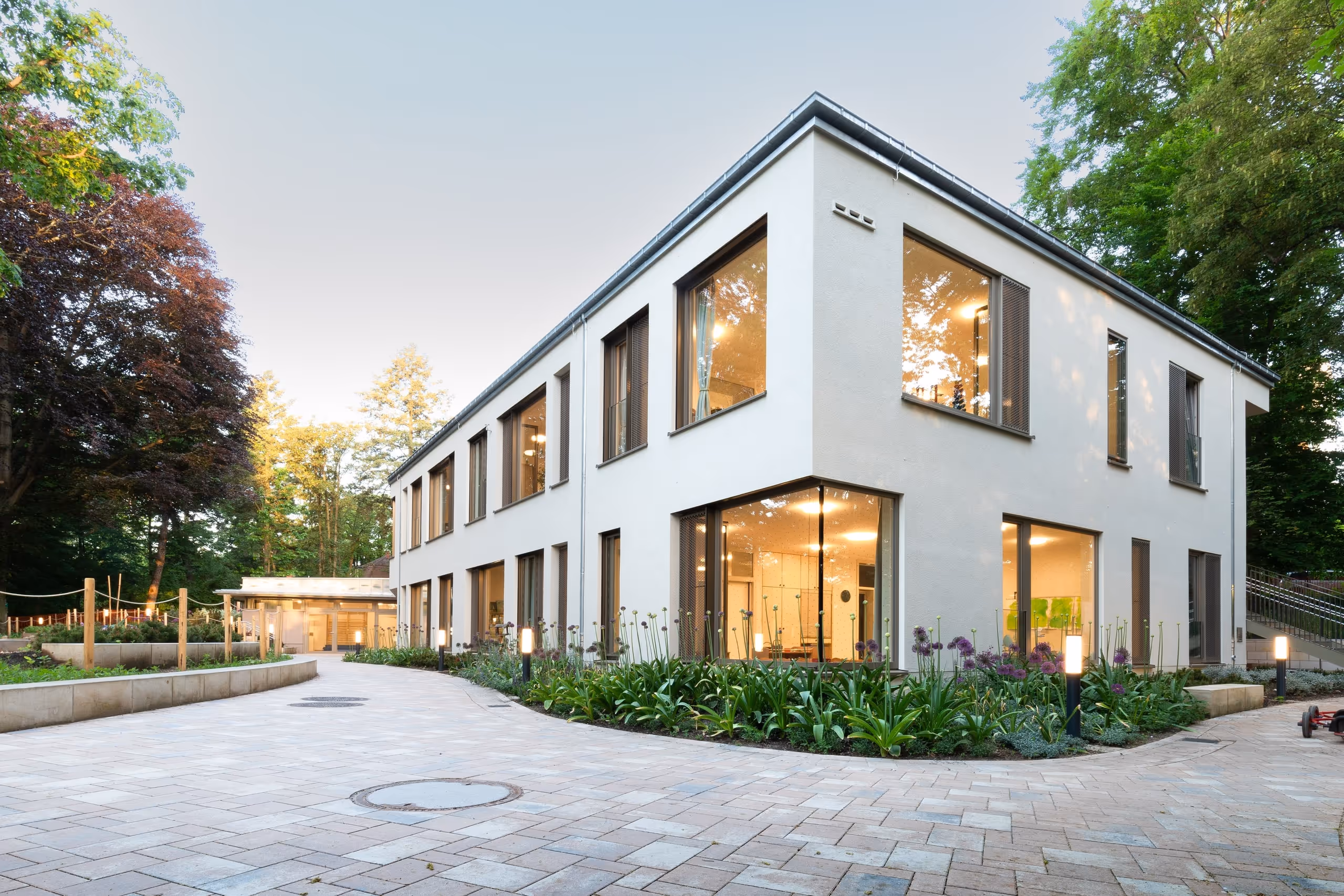 FRÖBEL-Kindergarten „Am Königswald“ in Dresden-Klotzsche: weißes Gebäude mit großen Fenstern und gepflastertem Vorplatz.
