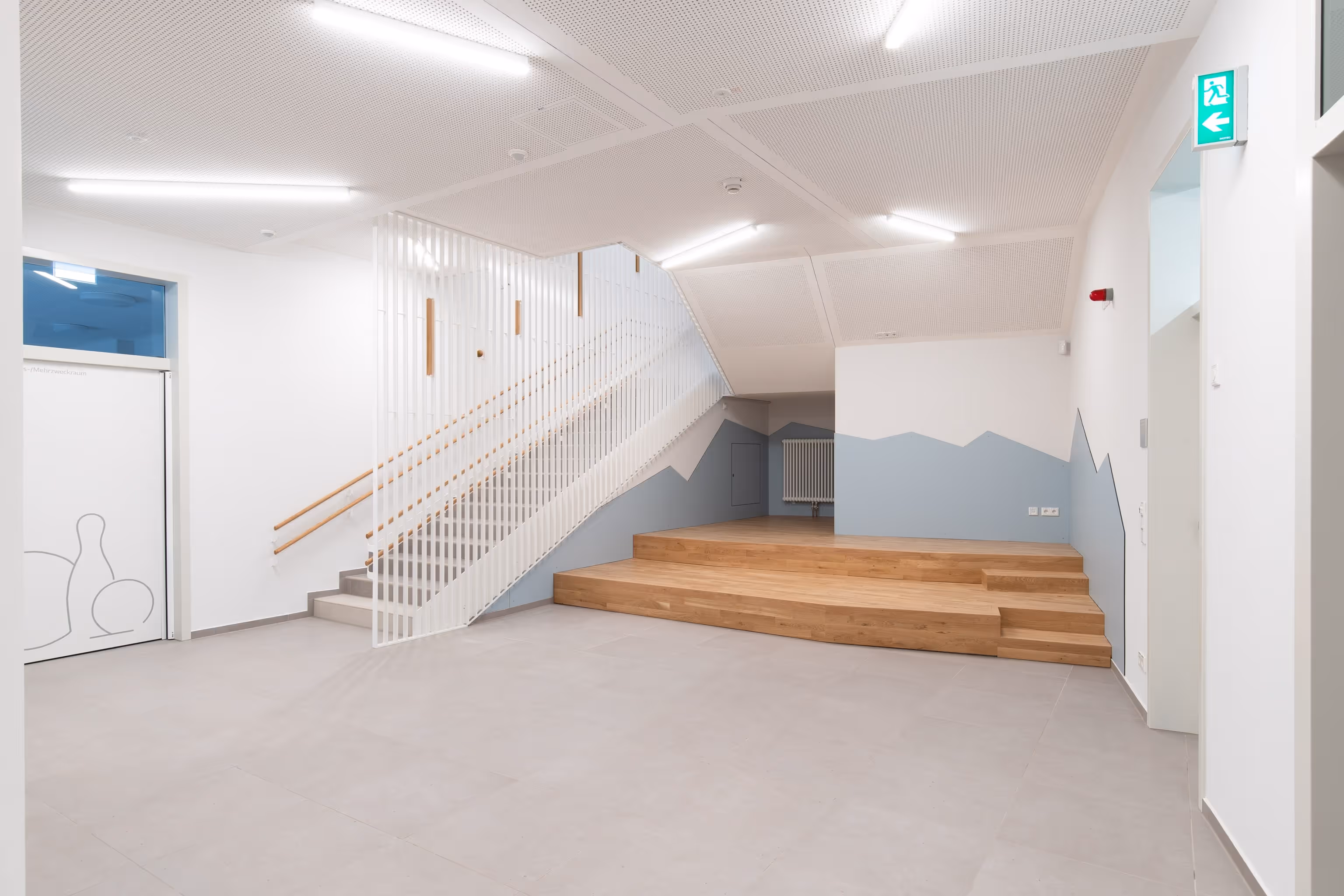 Heller Raum mit moderner Treppe, Holzbühne und blauer Wandgestaltung mit Bergen.