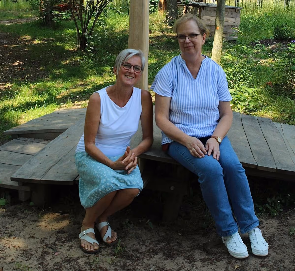 Zwei Mitarbeiterinnen des FRÖBEL-Kindergartens „Am Königswald“ sitzen auf einer Bank im Außengelände.