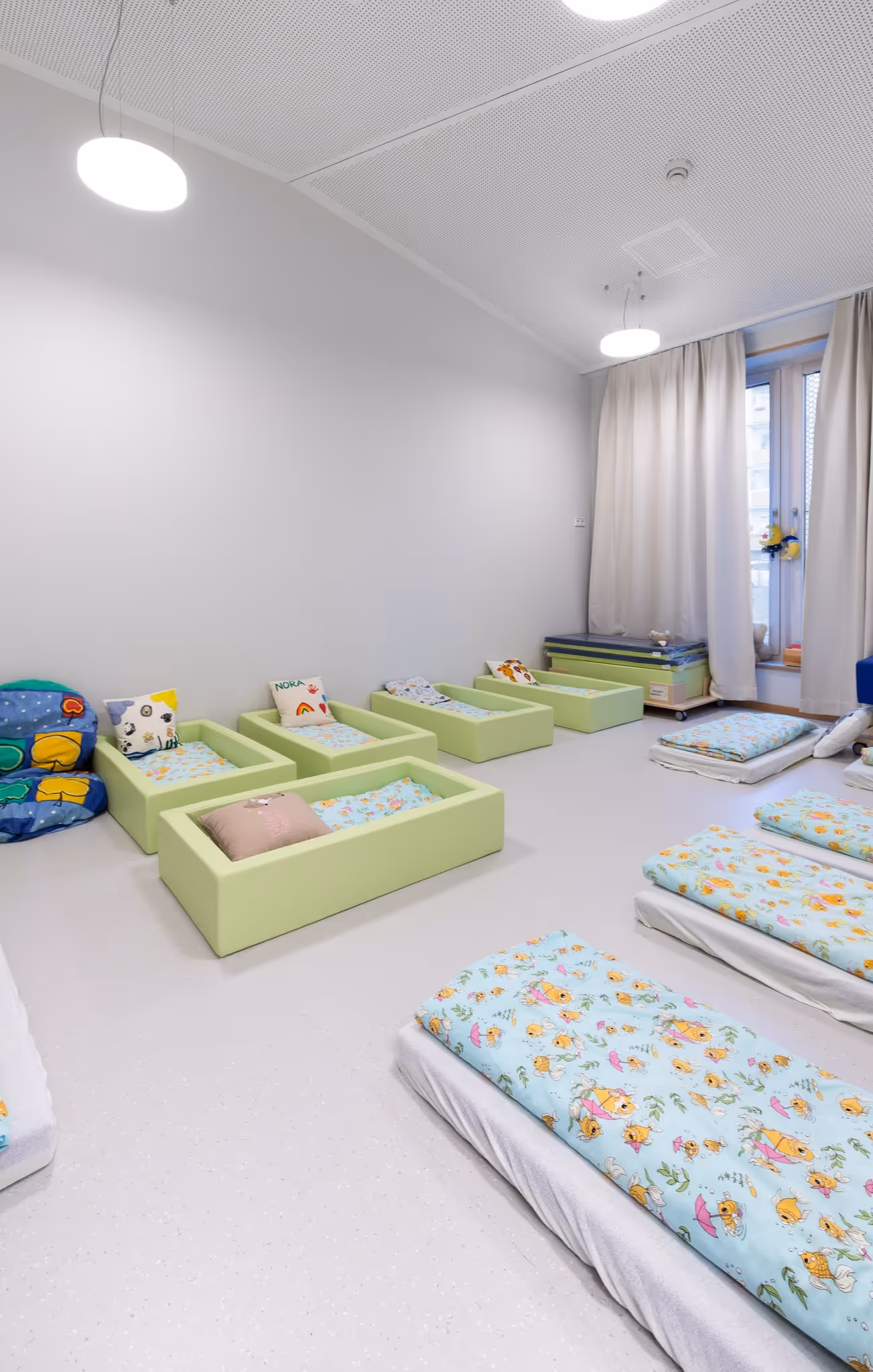 Kinder-Schlafraum mit kleinen Betten, Kissen und bunten Decken für den Mittagsschlaf.