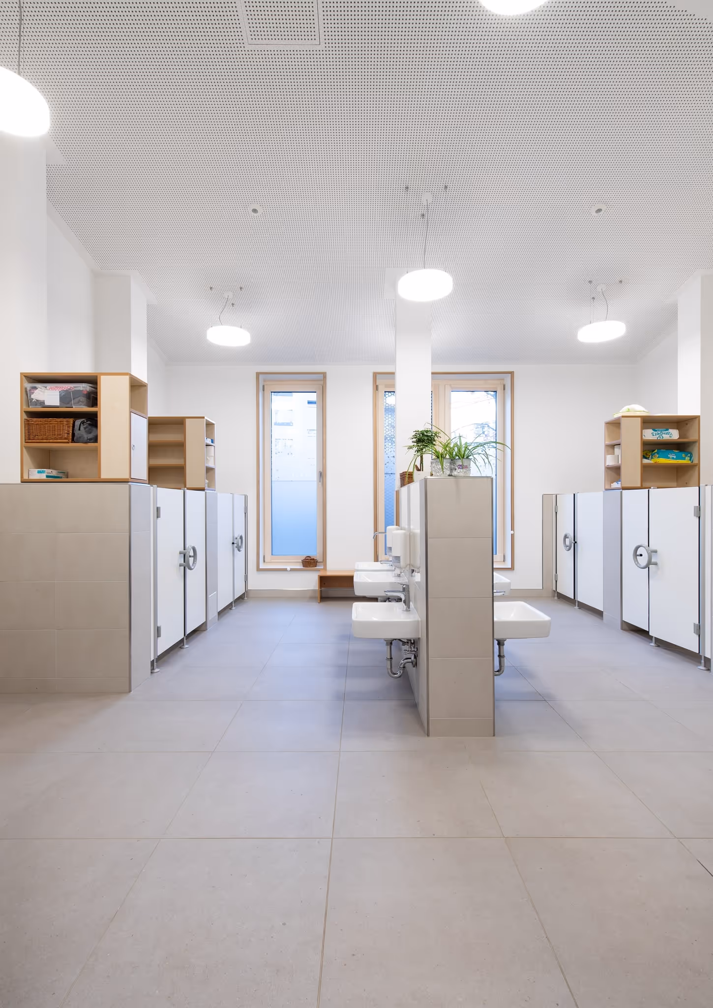 Helle, saubere Sanitäranlage mit mehreren Waschbecken und Toilettenkabinen in modernen Farben.