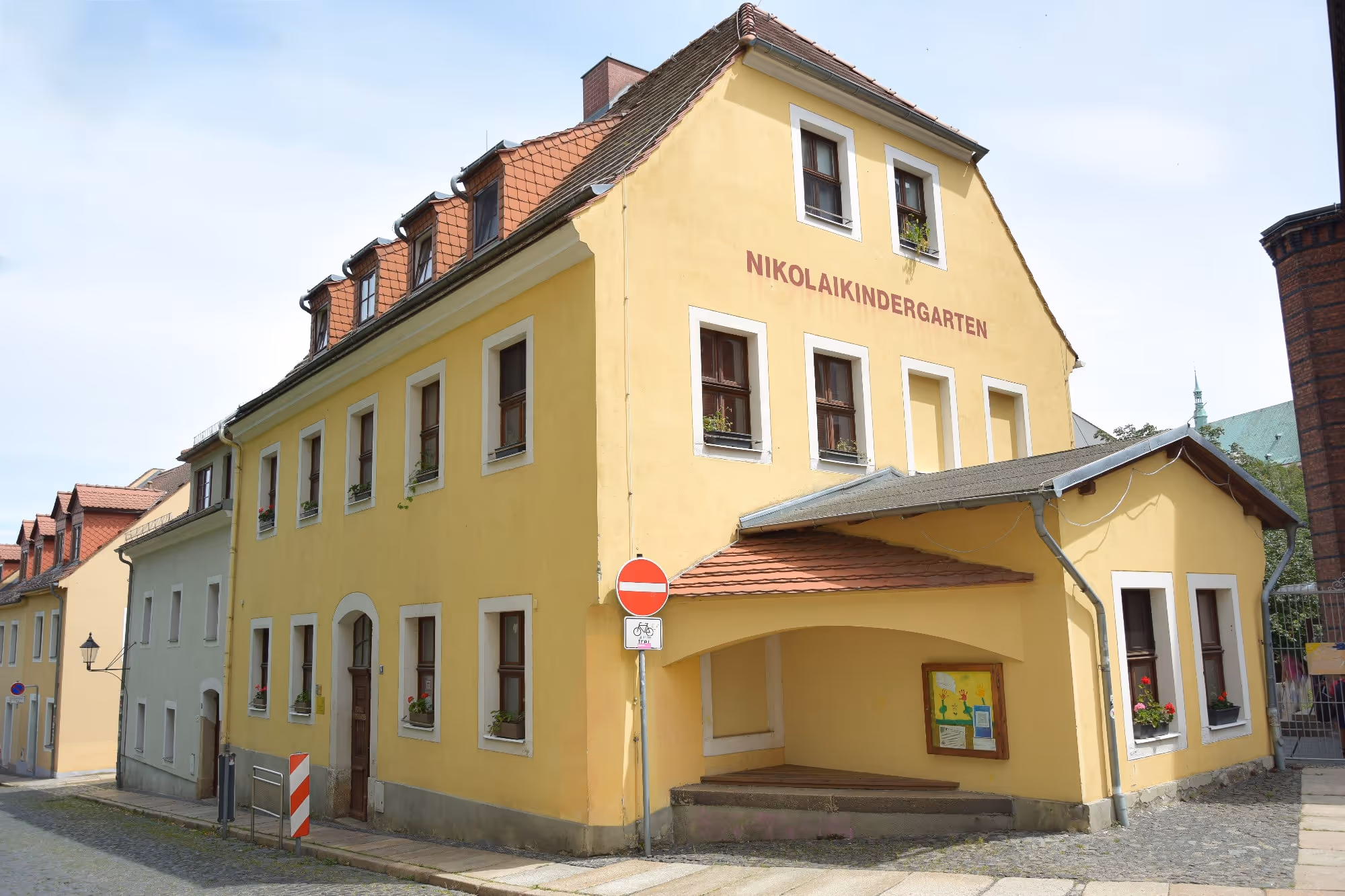 FRÖBEL-Kinderhaus „Nikolaivorstadt“ in Görlitz: gelbes Gebäude mit rotem Ziegeldach und dem Schriftzug Nikolaikindergarten.