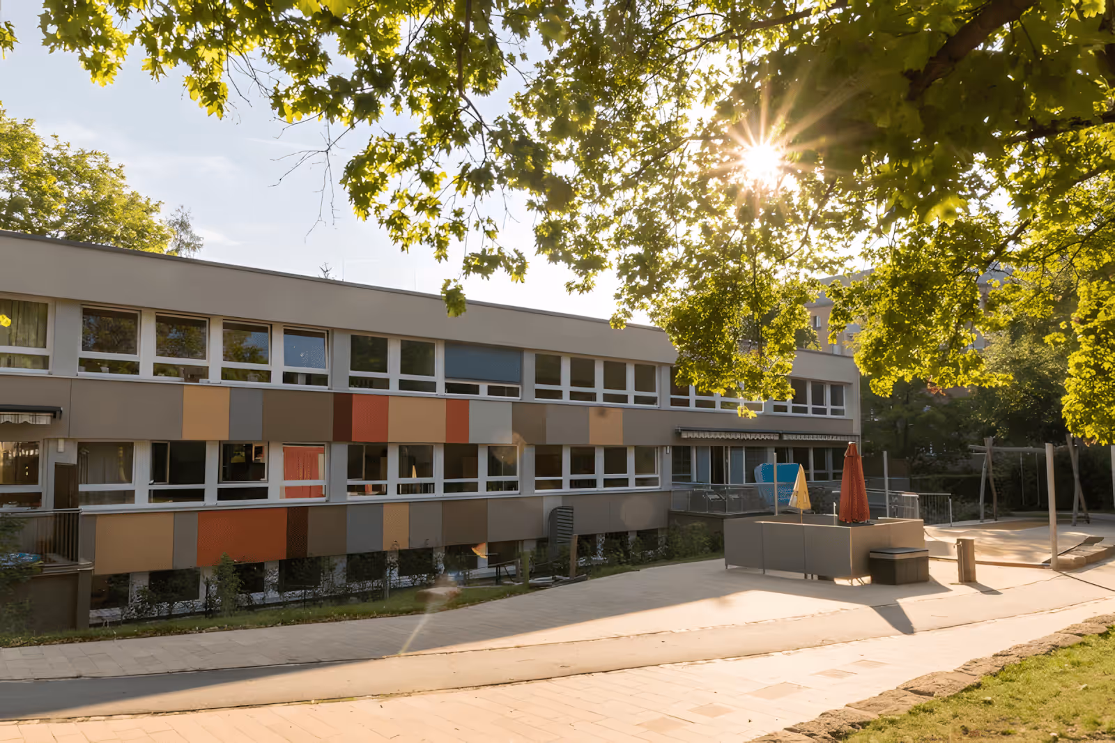 Sonnenlicht scheint durch Blätter auf ein modernes Gebäude mit bunten Paneelen und Außenbereich.