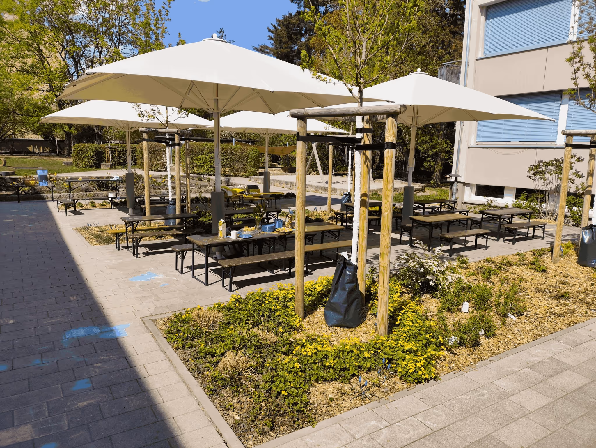 Terrasse mit Sonnenschirmen, Bänken und Tischen vor dem Kinderhaus Rosa-Menzer-Straße.