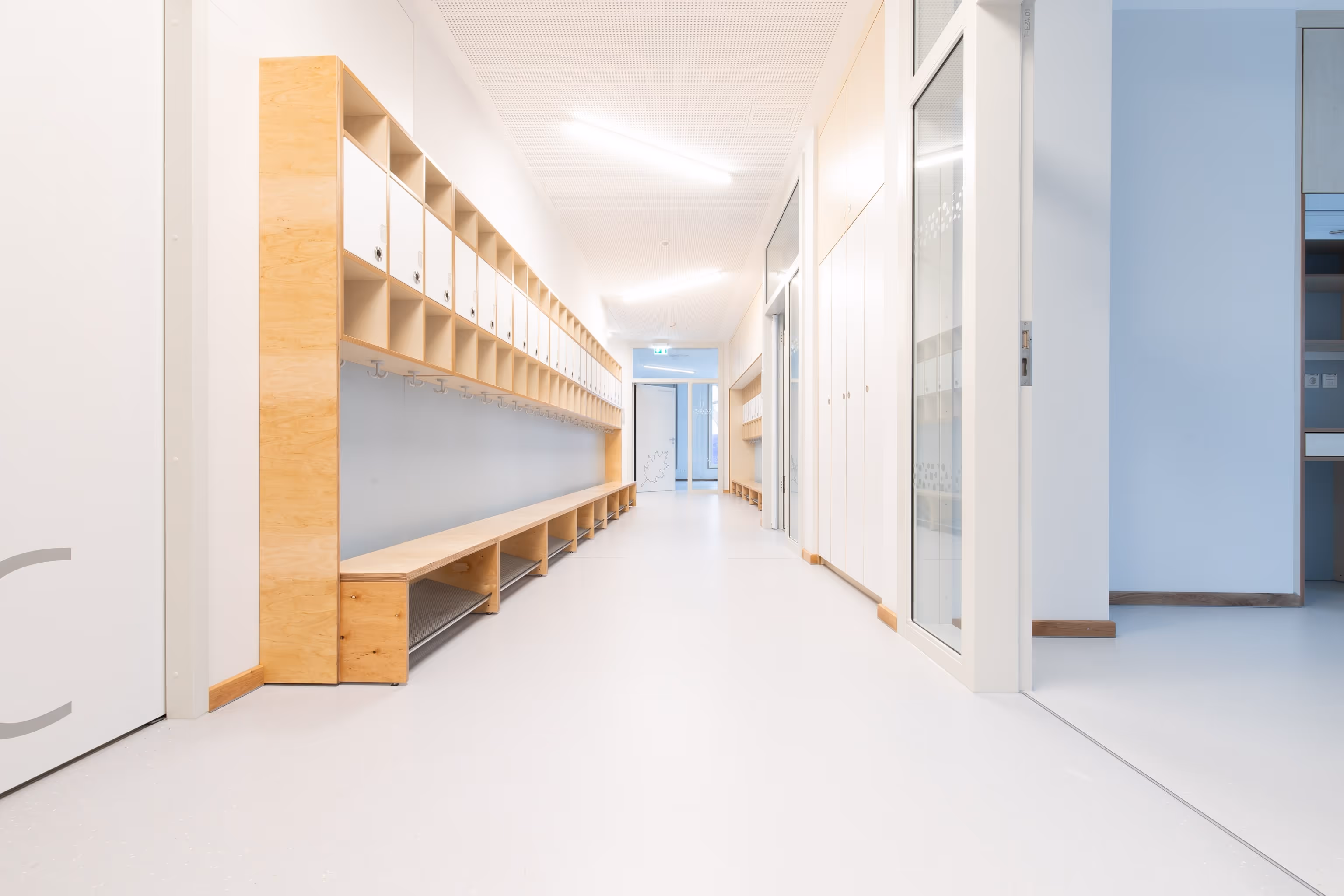 Moderner heller Flur mit Holzschränken, Sitzbank und Garderobenhaken in einer Schule oder Kita